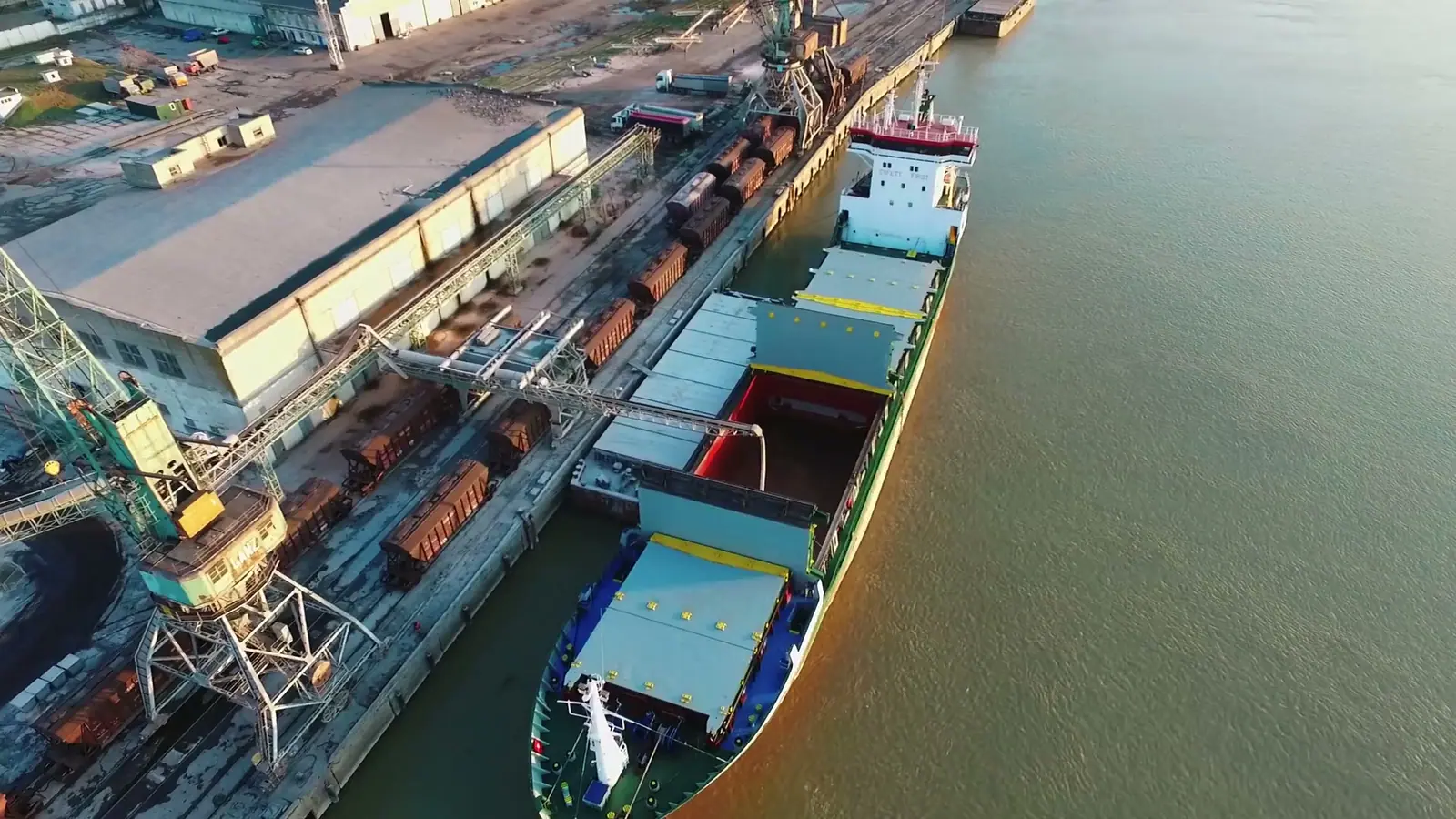Aerial view of a general cargo ship loading at a quay stacked with timber and steel
