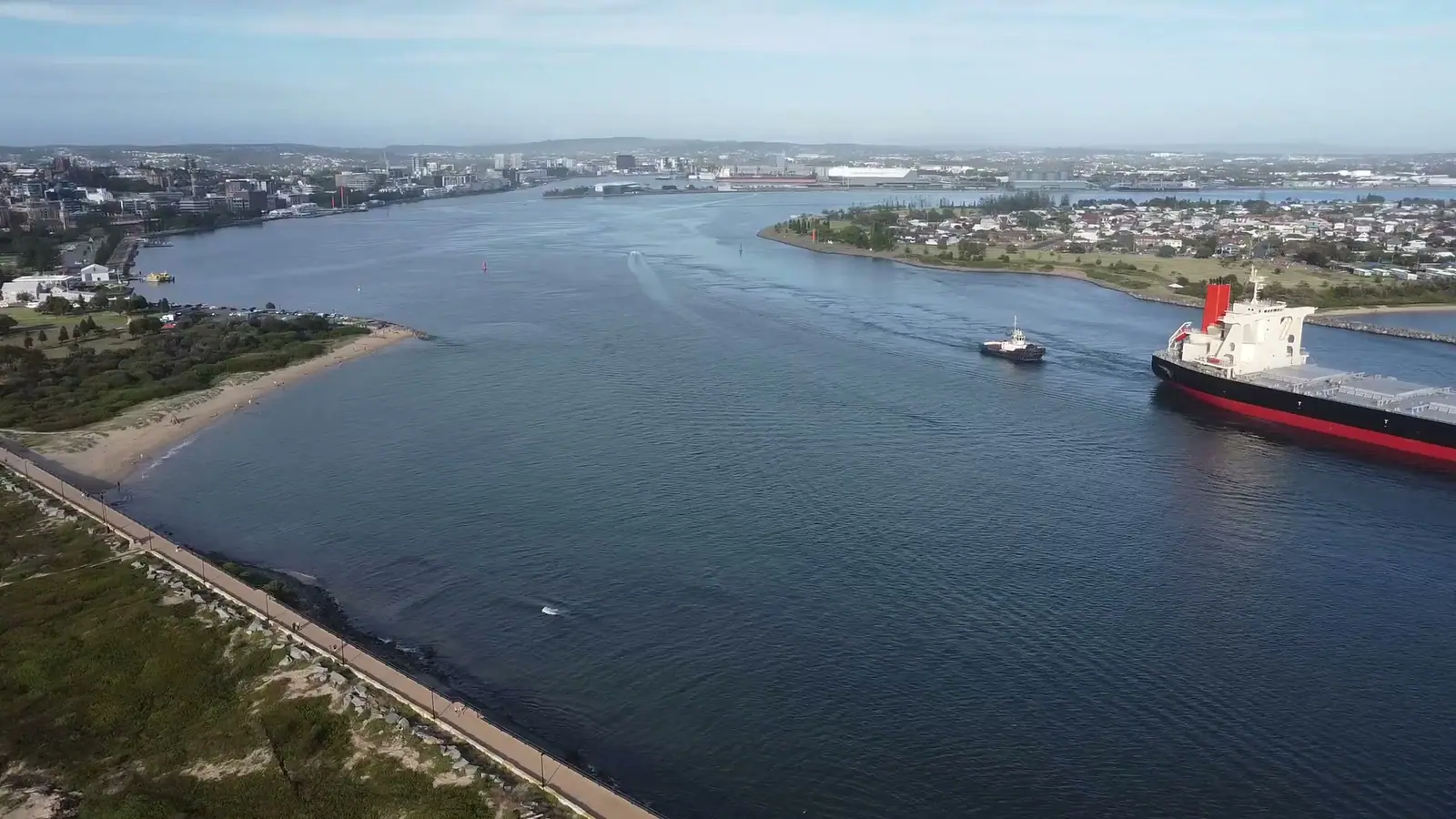 Aerial view of a bulk carrier leaving harbour escorted by tugs