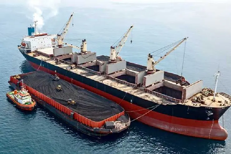Bulk carrier with deck cranes transferring cargo to a barge at sea