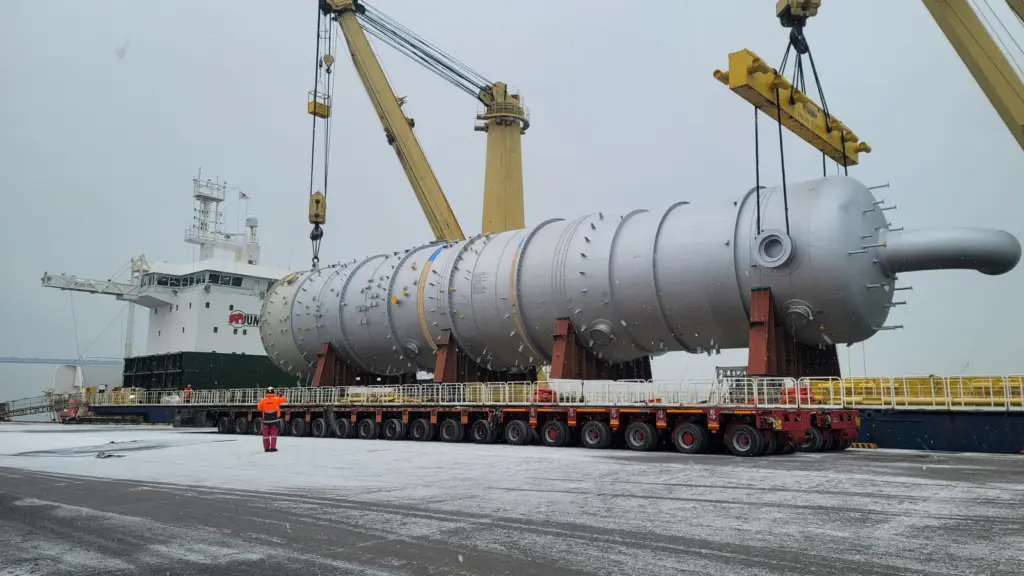 Process column on modular trailers at the quayside, beneath a ship's cranes