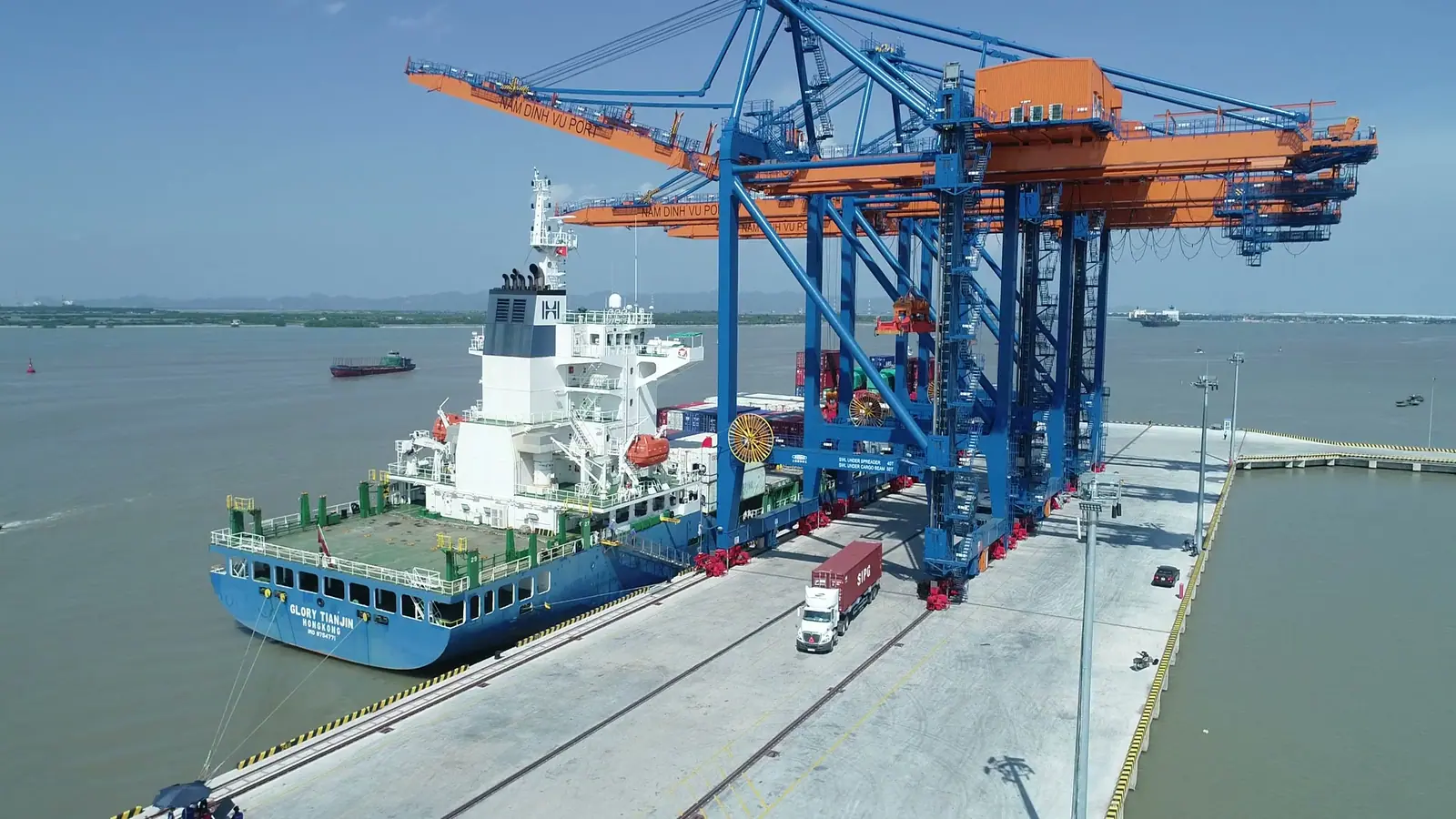 Aerial view of a container ship under gantry cranes, with a truck on the pier