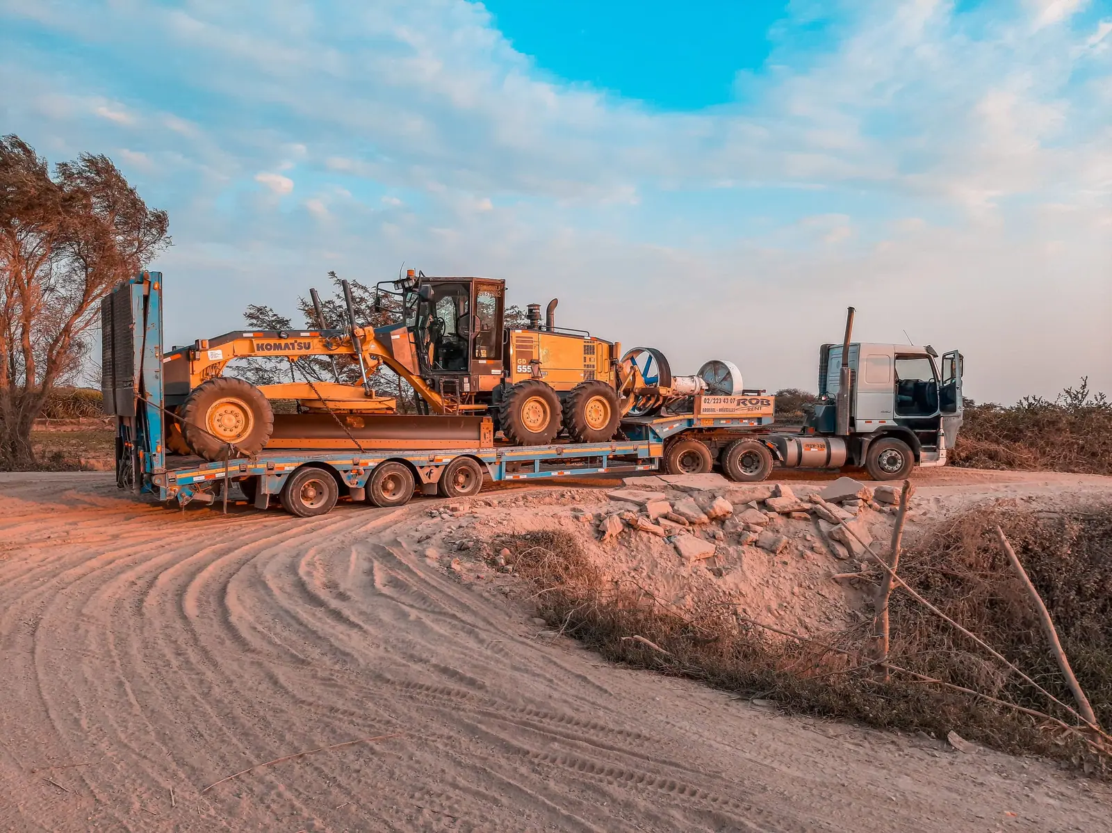 Motor grader loaded on a multi-axle low-bed trailer at sunset