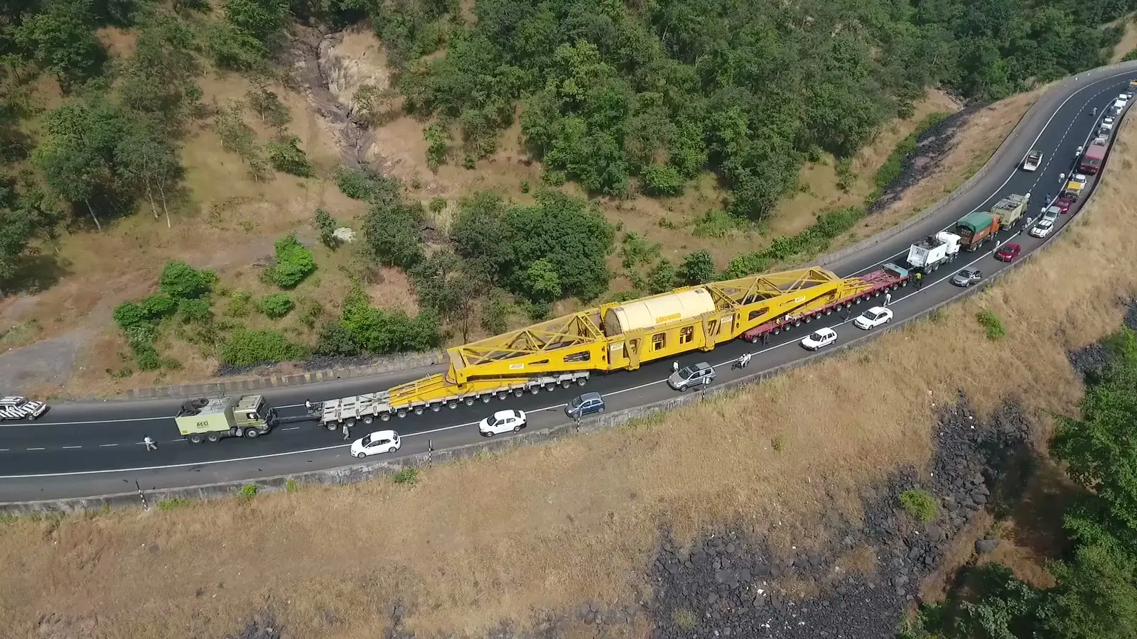Aerial view of a pressure vessel on a multi-axle beam trailer climbing a winding hill road