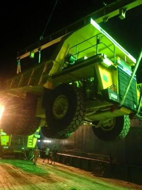 Mining dump truck lifted by a ship's crane at night