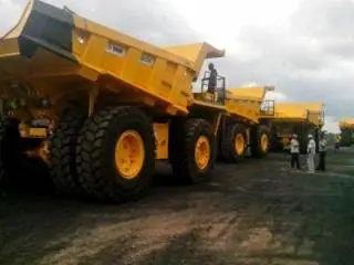 Row of yellow mining dump trucks parked on site