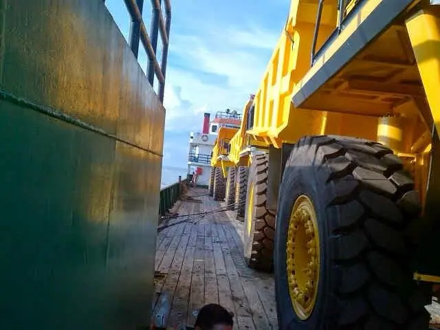 Mining dump trucks lined up on a barge beside the hull