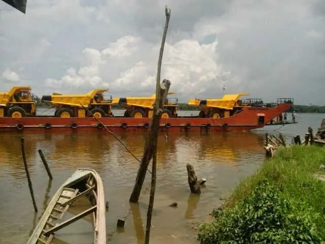 Barge carrying a row of mining dump trucks on a river
