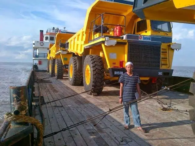 Worker standing beside mining dump trucks on a barge