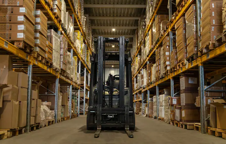 Forklift in a warehouse aisle lined with stacked cartons